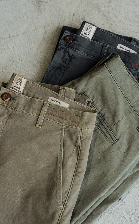 Three pairs of pants stacked on a textured surface