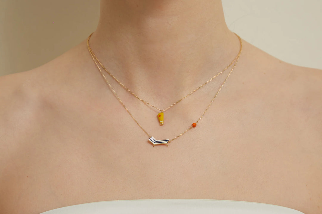 Two gold necklaces with small pendants on a neutral background