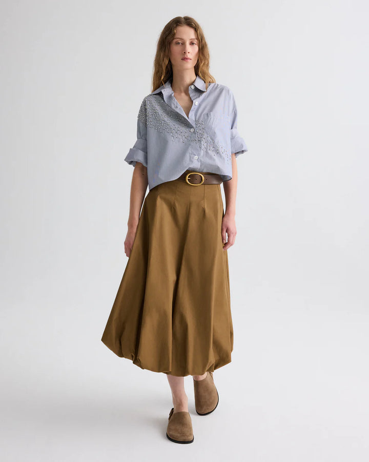 Woman wearing a light blue shirt and brown skirt on a white background