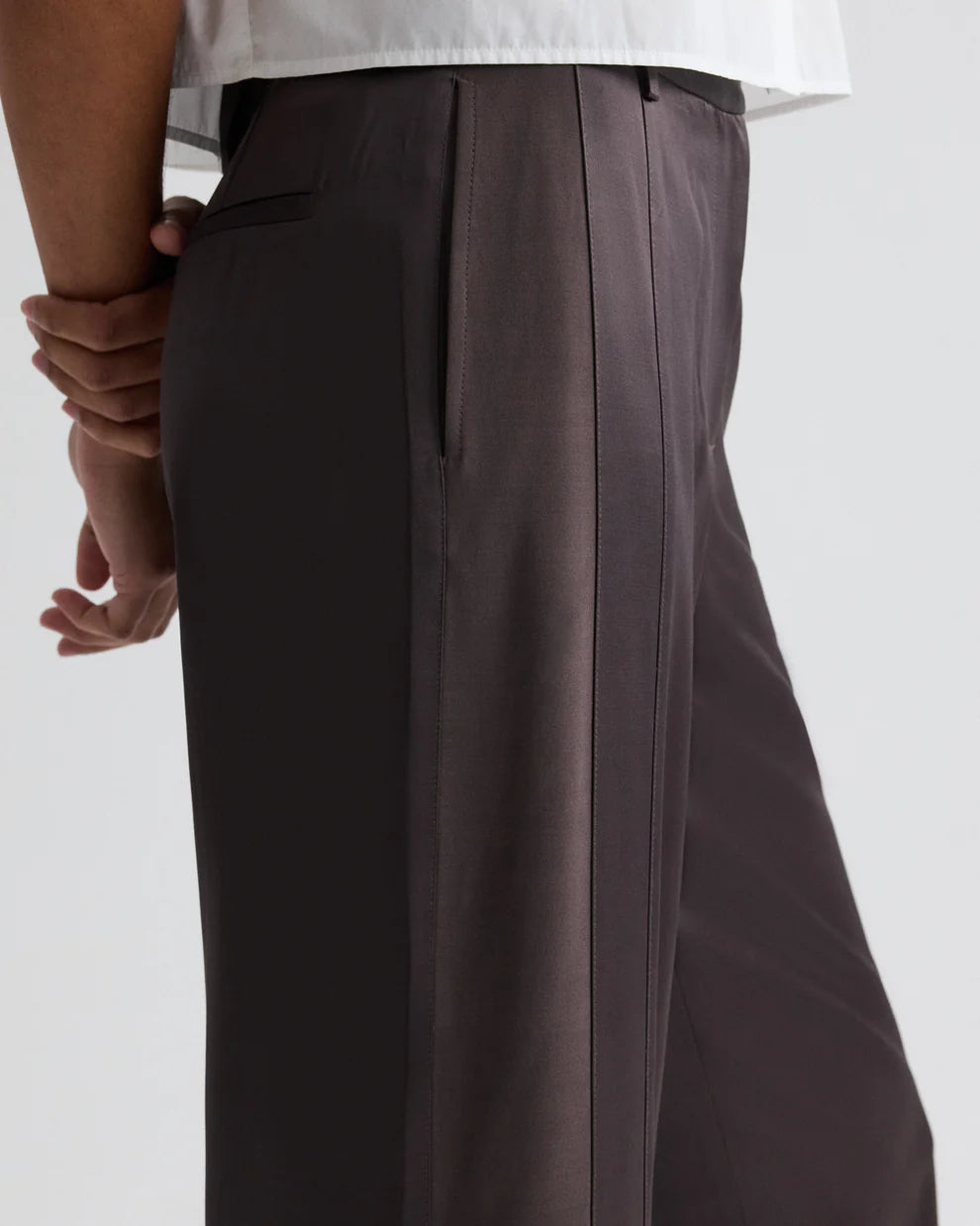Brown pleated pants worn by a person on a white background