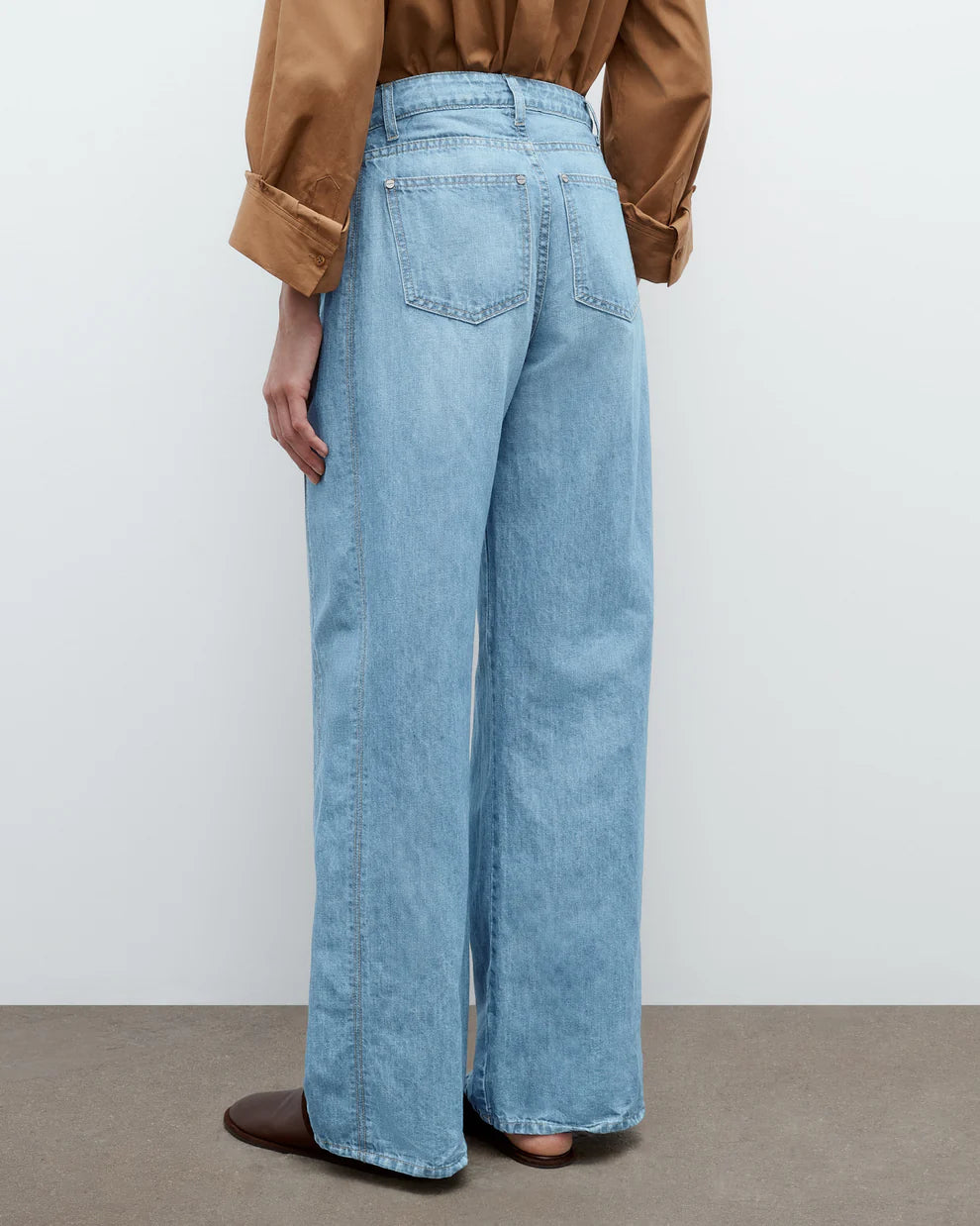 Person wearing light blue jeans and a brown jacket on a plain background