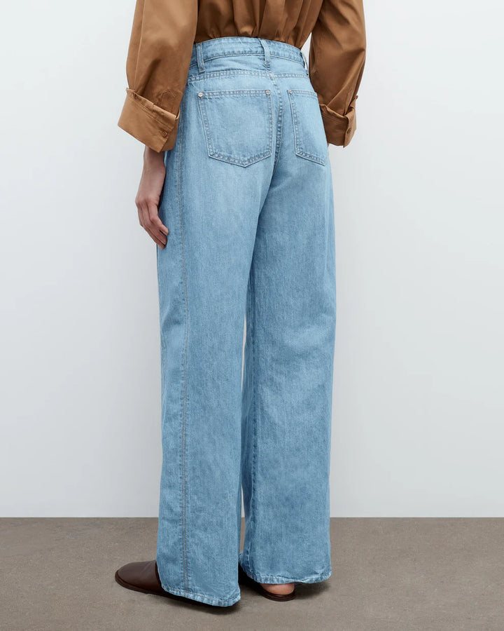 Person wearing light blue jeans and a brown jacket on a plain background