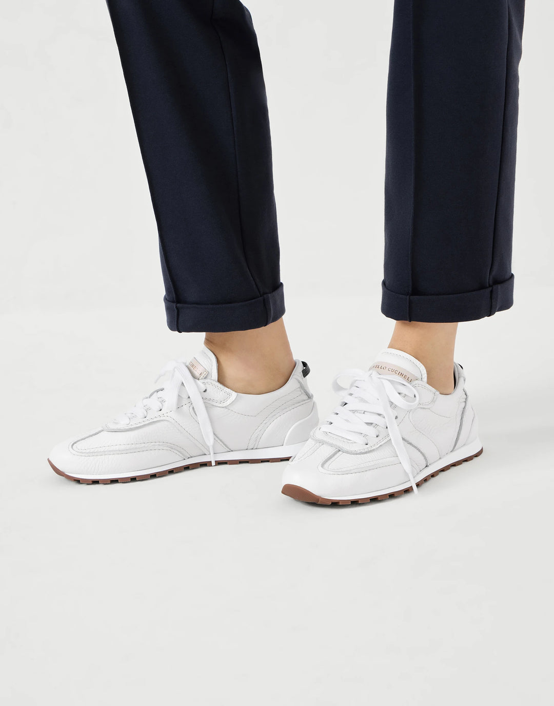 White sneakers worn with navy pants on a light gray background
