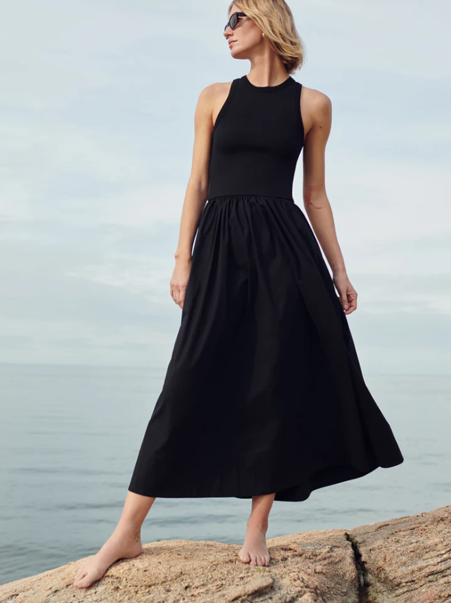 Woman in a black dress standing on a rock by the water