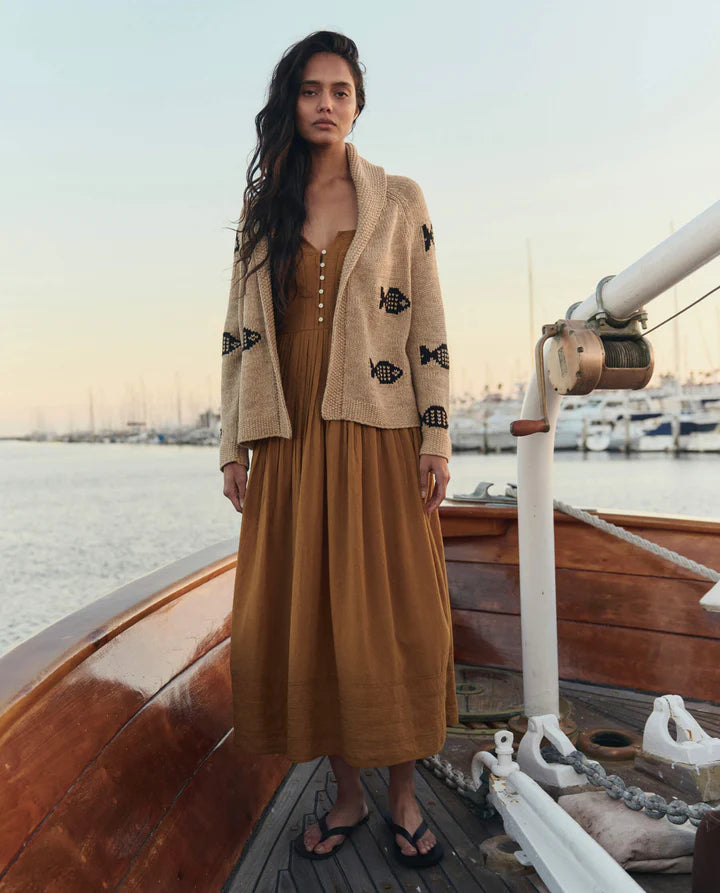 Woman in a mustard dress and beige cardigan on a boat with a waterfront background