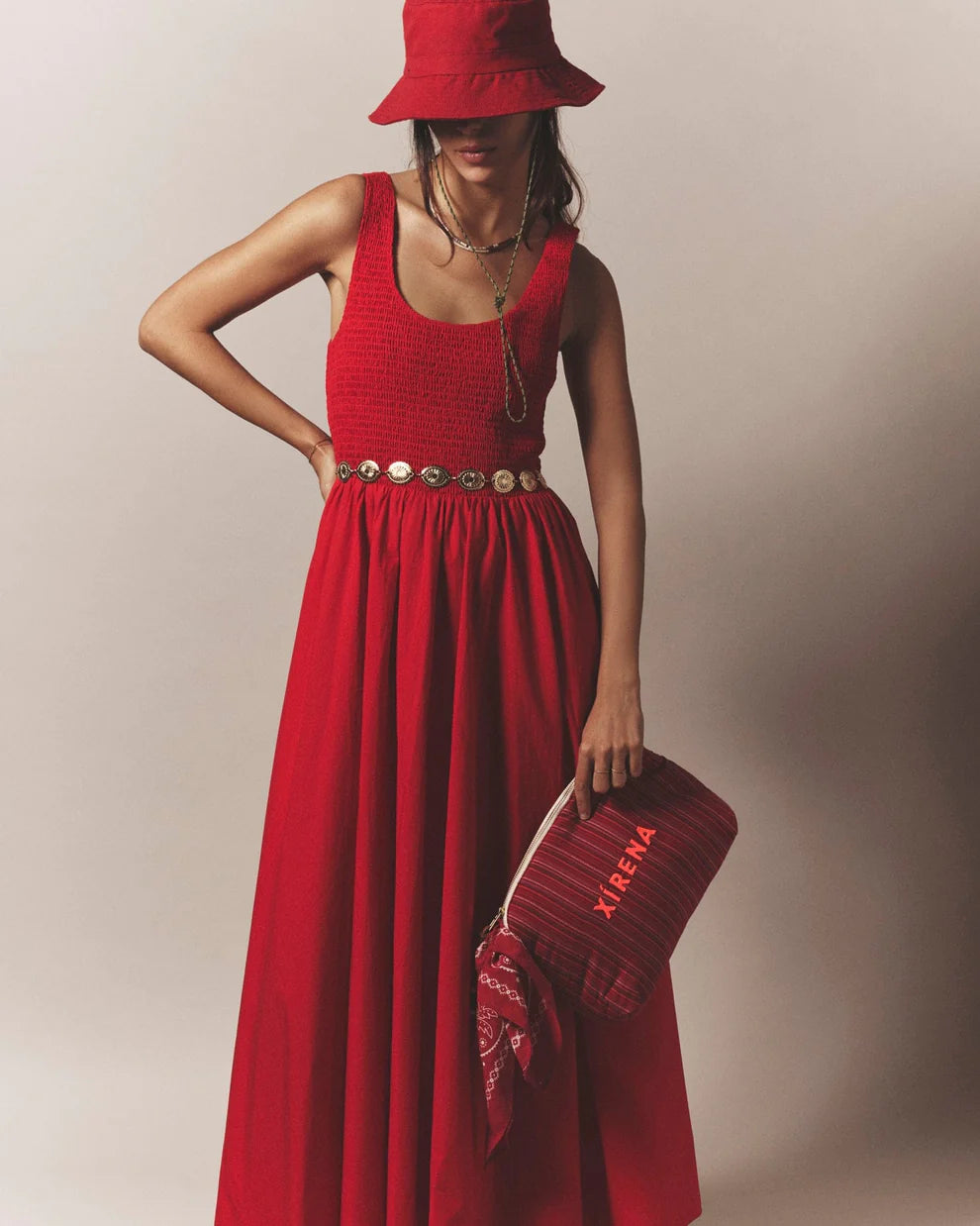 Woman in a red dress and hat holding a matching handbag against a plain background