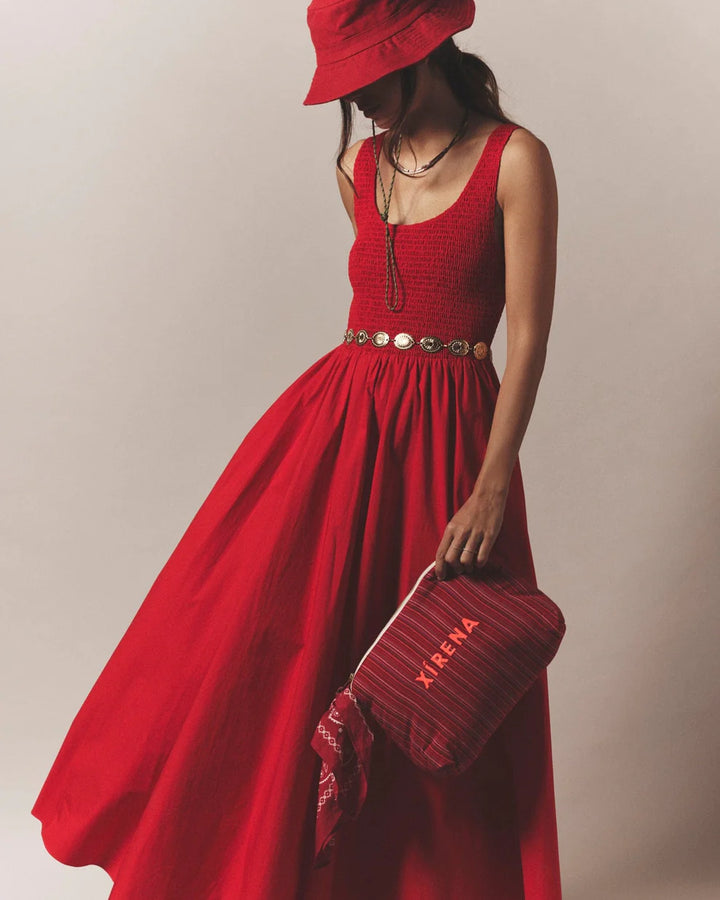 Woman in a red dress holding a matching red handbag against a neutral background