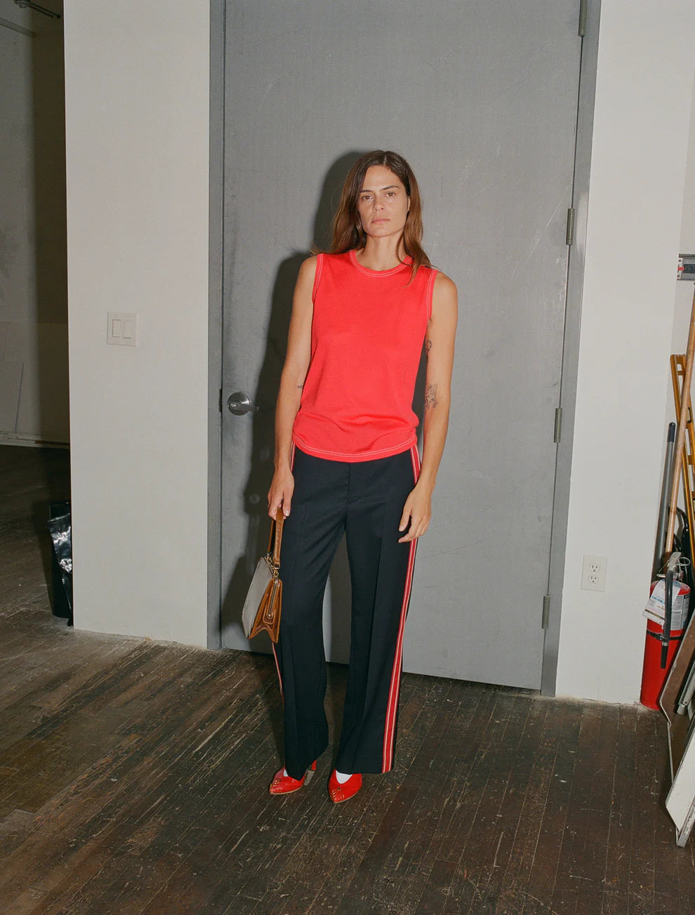 Woman in a red sleeveless top and black pants with red stripes standing in a room.