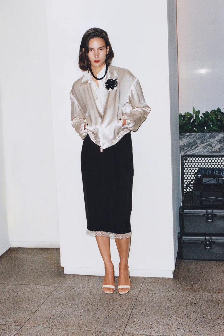 Woman in a stylish outfit with a metallic jacket and black skirt against a white wall.