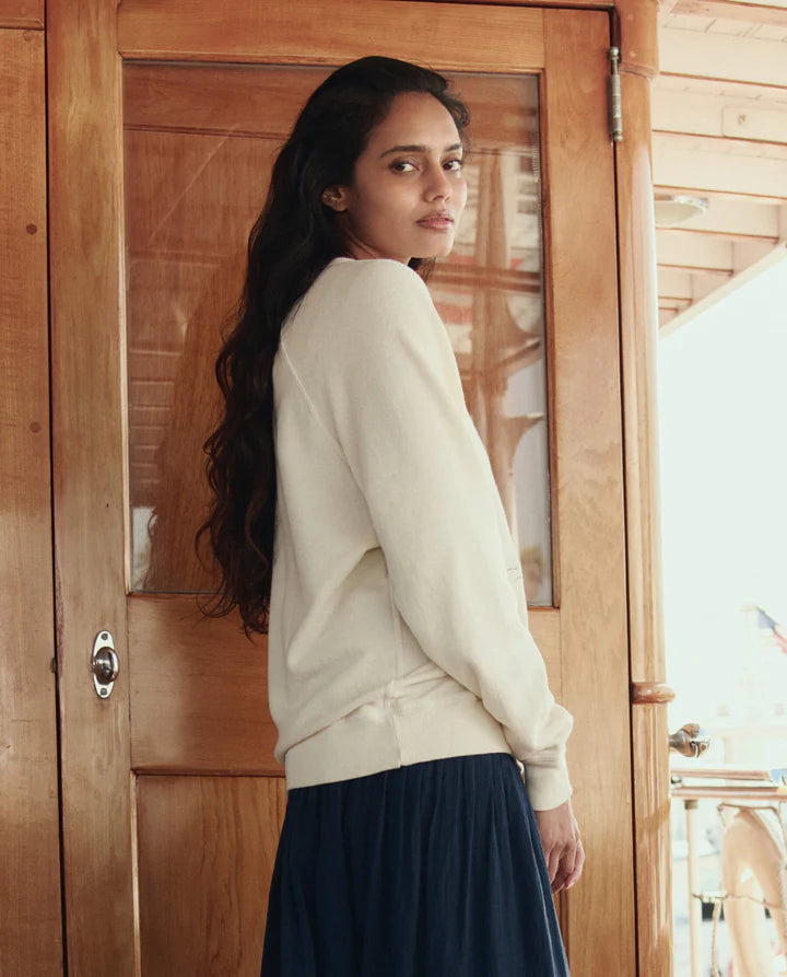 Woman in a white sweater and dark skirt standing in front of a wooden door.