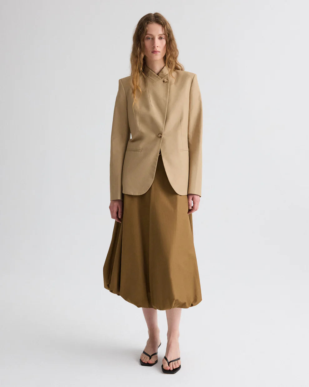 Woman wearing a beige blazer and skirt set on a white background