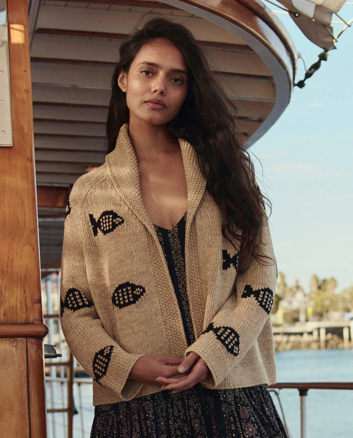 Woman wearing a beige cardigan with black patterns on a boat deck.