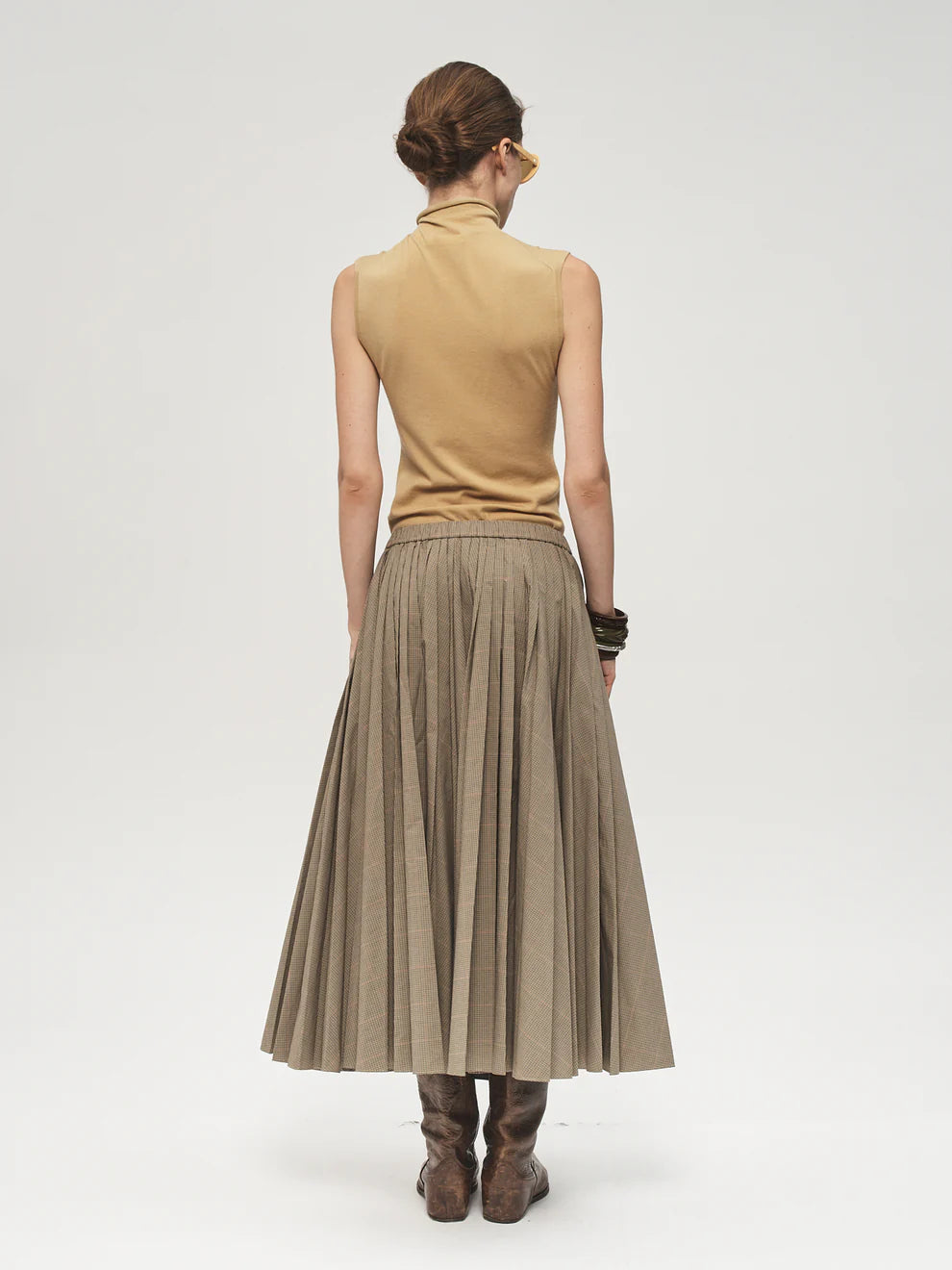 Woman wearing a beige sleeveless top and pleated skirt on a white background