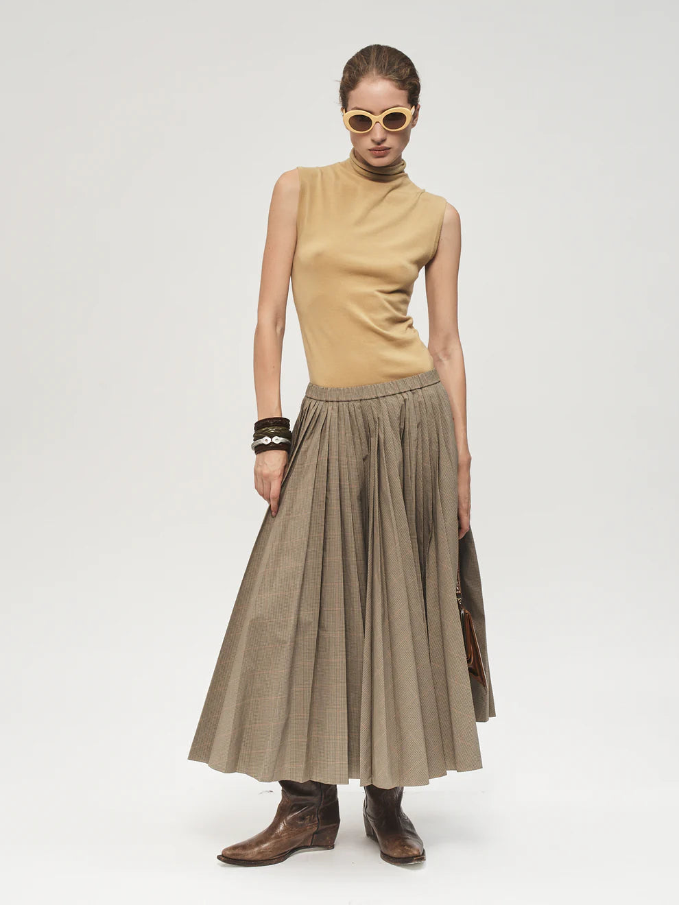Woman wearing a beige sleeveless top and pleated skirt on a white background