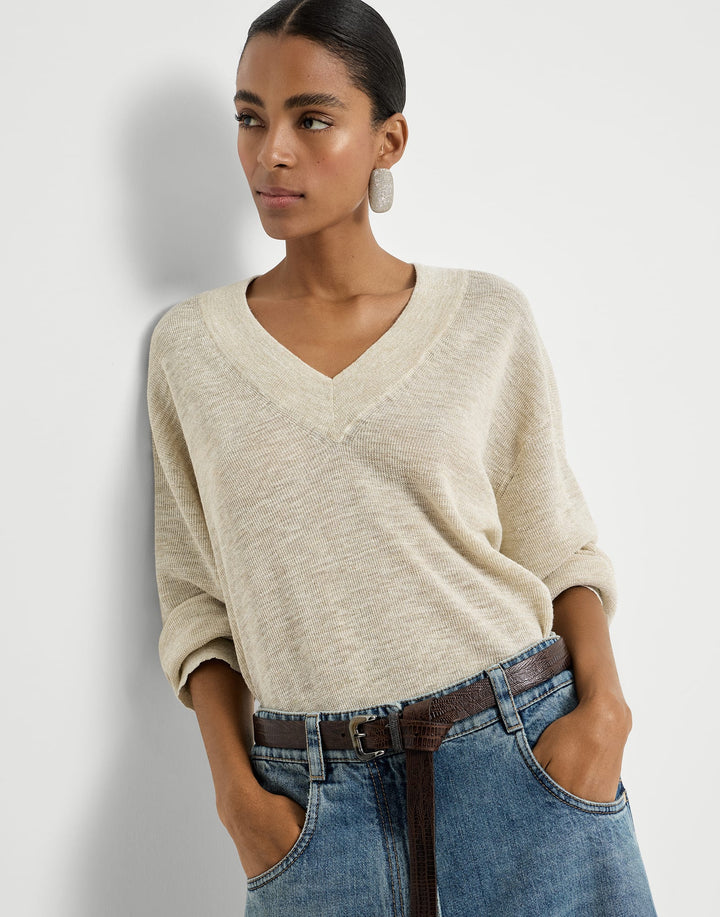 Woman wearing a beige sweater and blue jeans against a plain background
