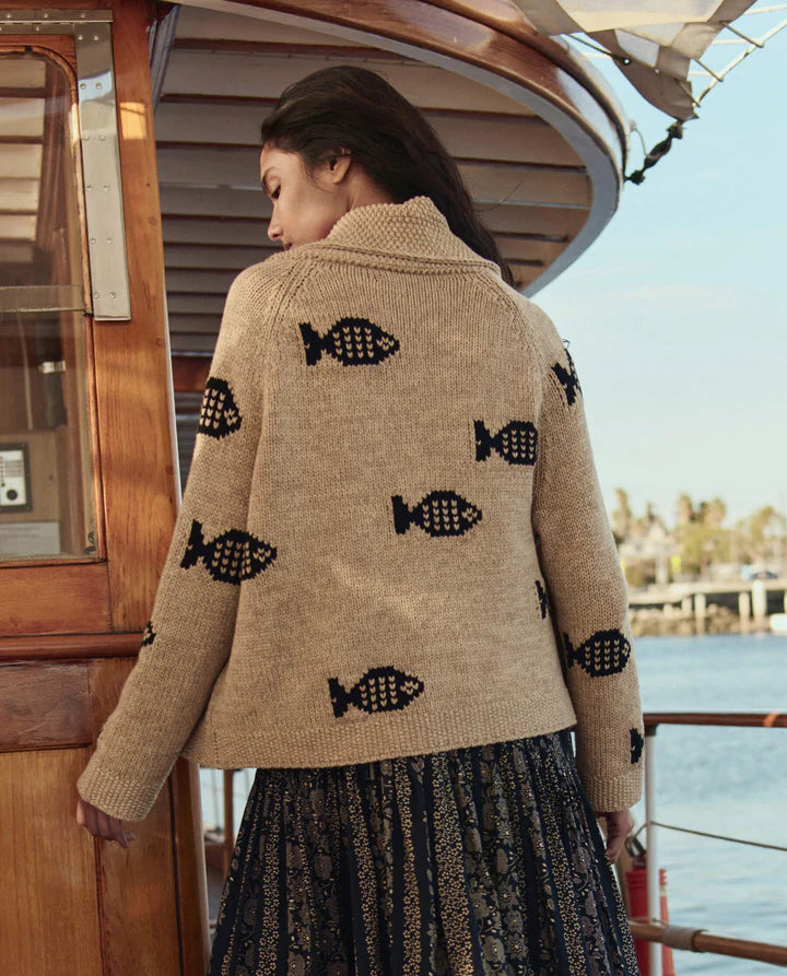 Woman wearing a beige sweater with black fish patterns on a boat.