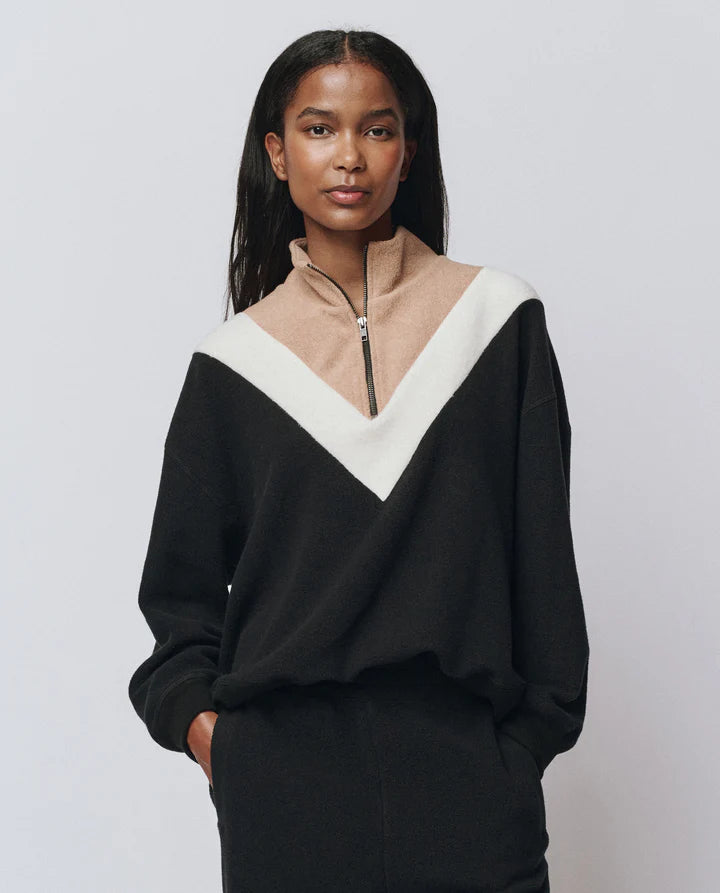 Woman wearing a black and beige color-blocked sweater against a plain background