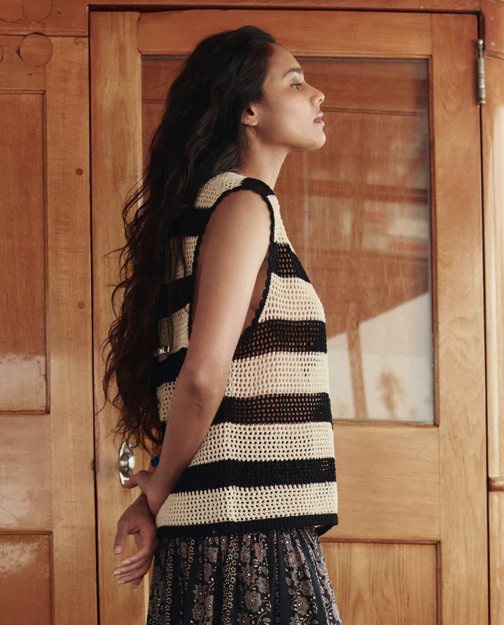 Woman wearing a black and white striped crochet top in front of a wooden door.