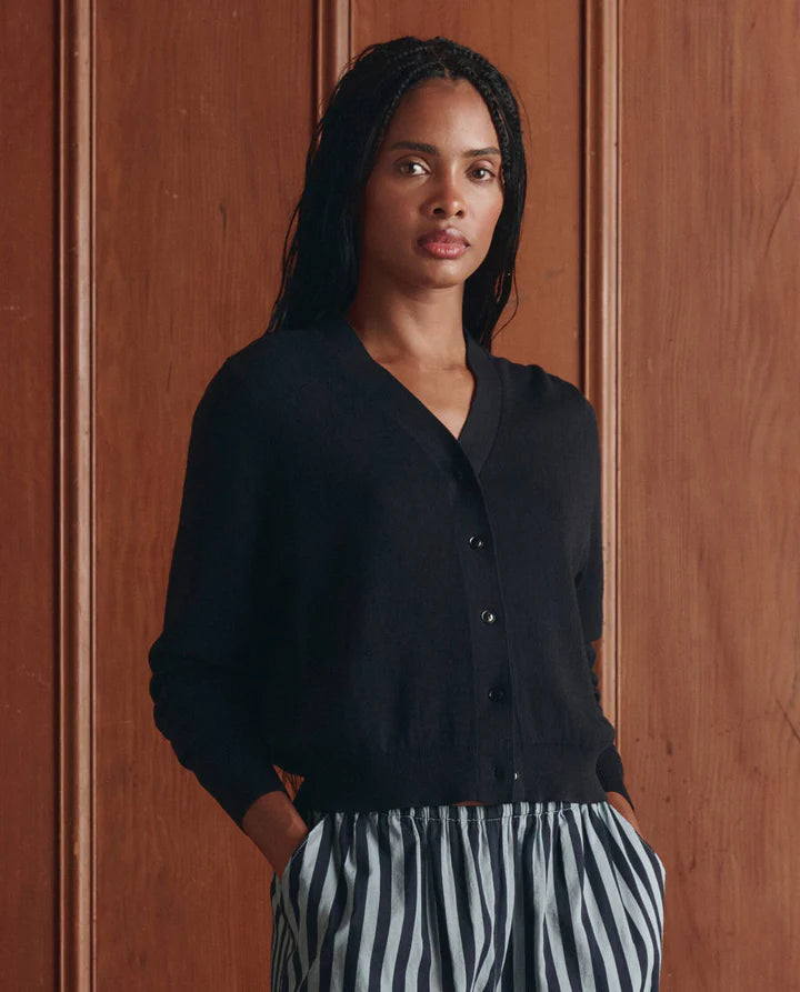 Woman wearing a black cardigan and striped pants against a wooden wall