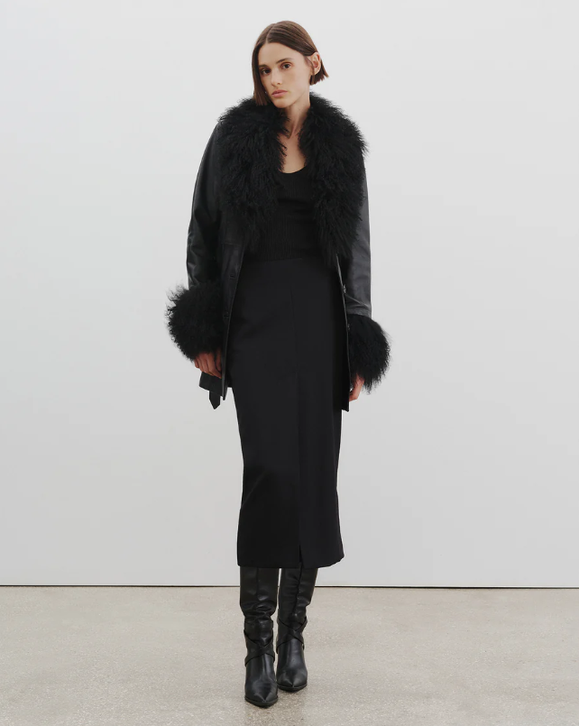Woman wearing a black coat with fur trim against a white background