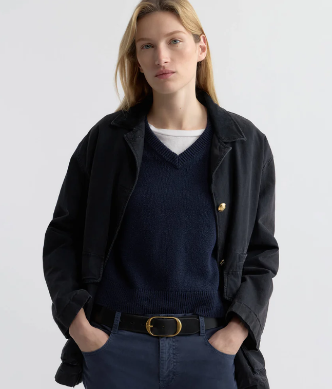 Woman wearing a black jacket over a navy sweater on a light gray background