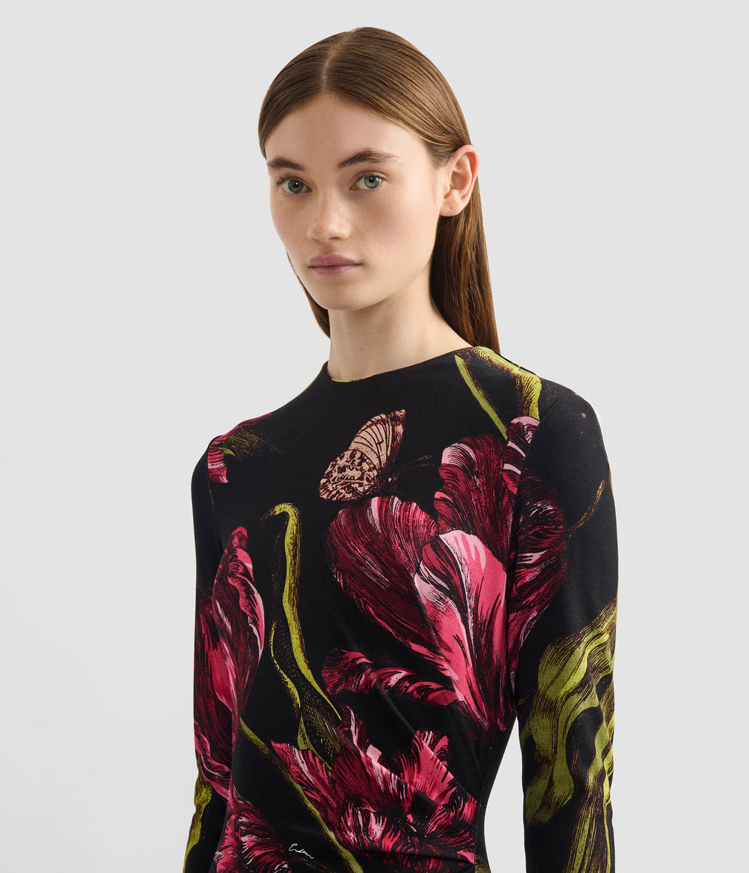 Woman wearing a black long-sleeve top with pink floral pattern on a light gray background