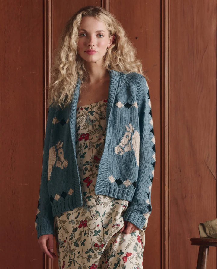 Woman wearing a blue cardigan with unicorn patterns against a wooden background