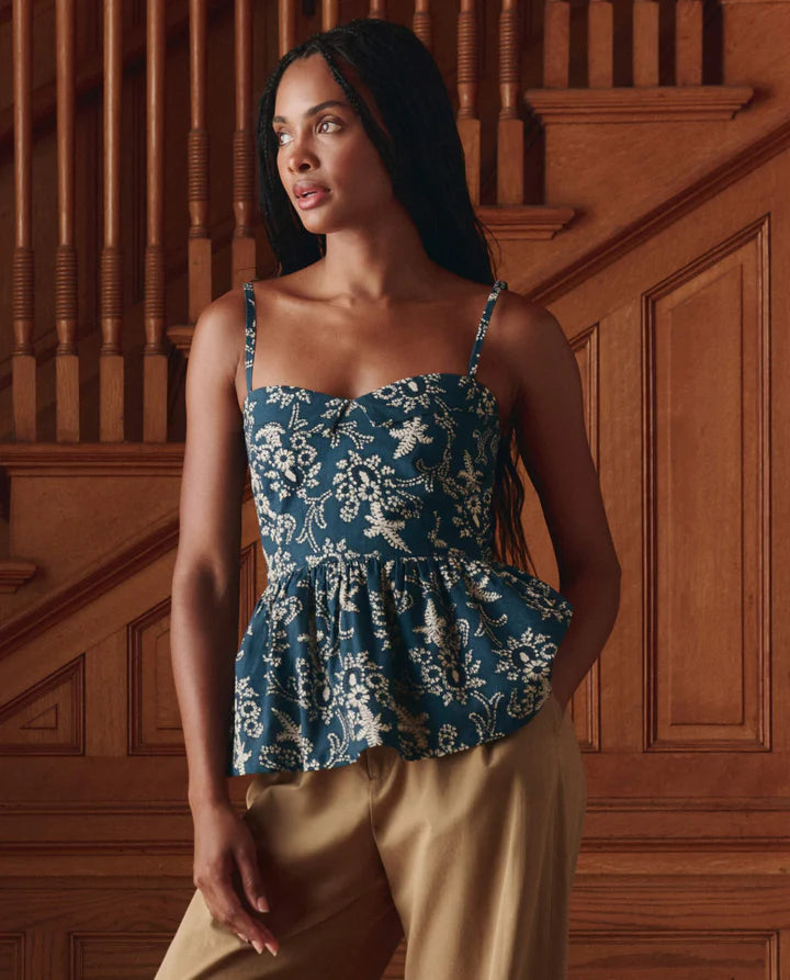 Woman wearing a blue floral peplum top and beige pants in a wooden interior setting