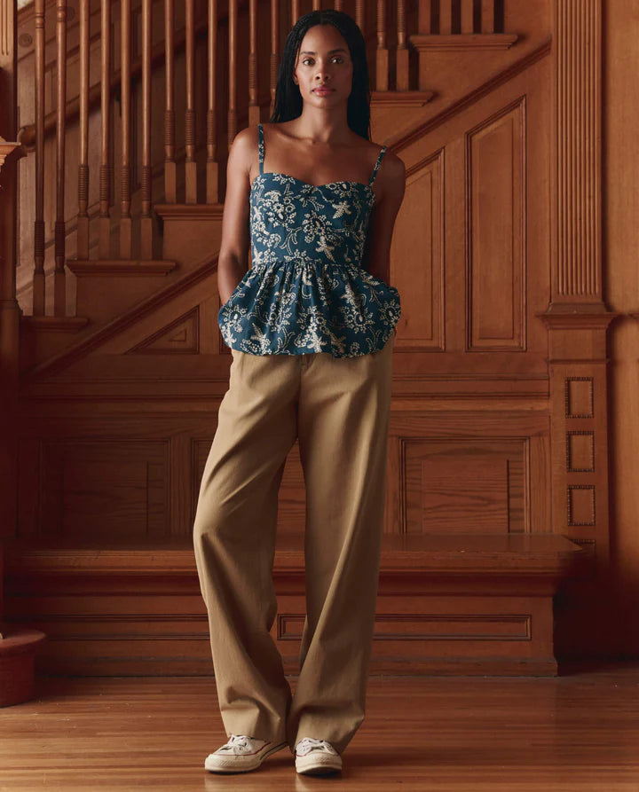 Woman wearing a blue floral top and beige pants standing in a wooden interior setting.
