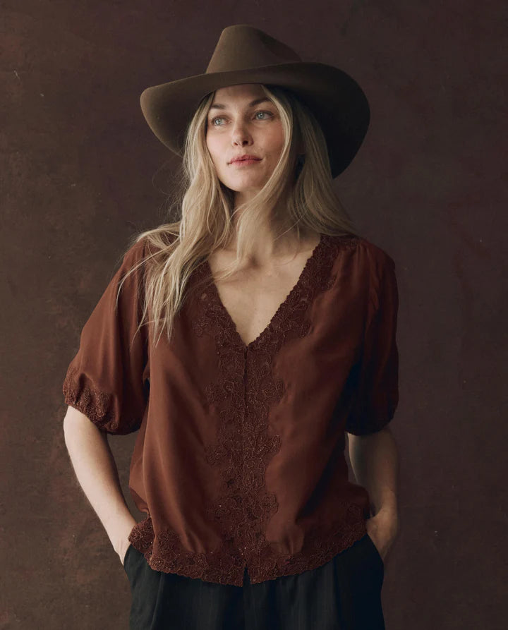 Woman wearing a brown blouse and hat against a dark background