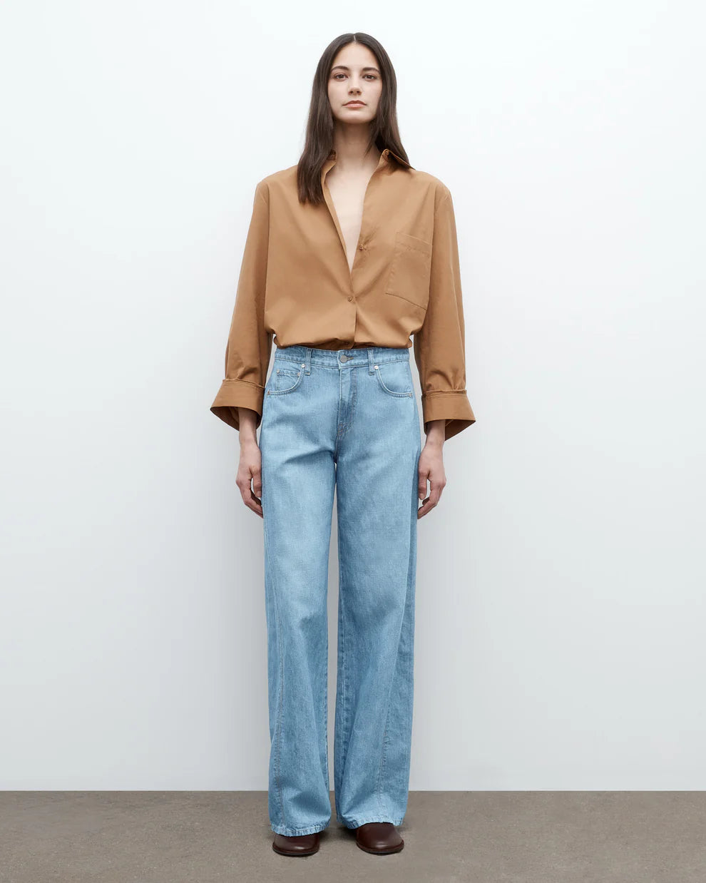 Woman wearing a brown blouse and light blue jeans against a white background