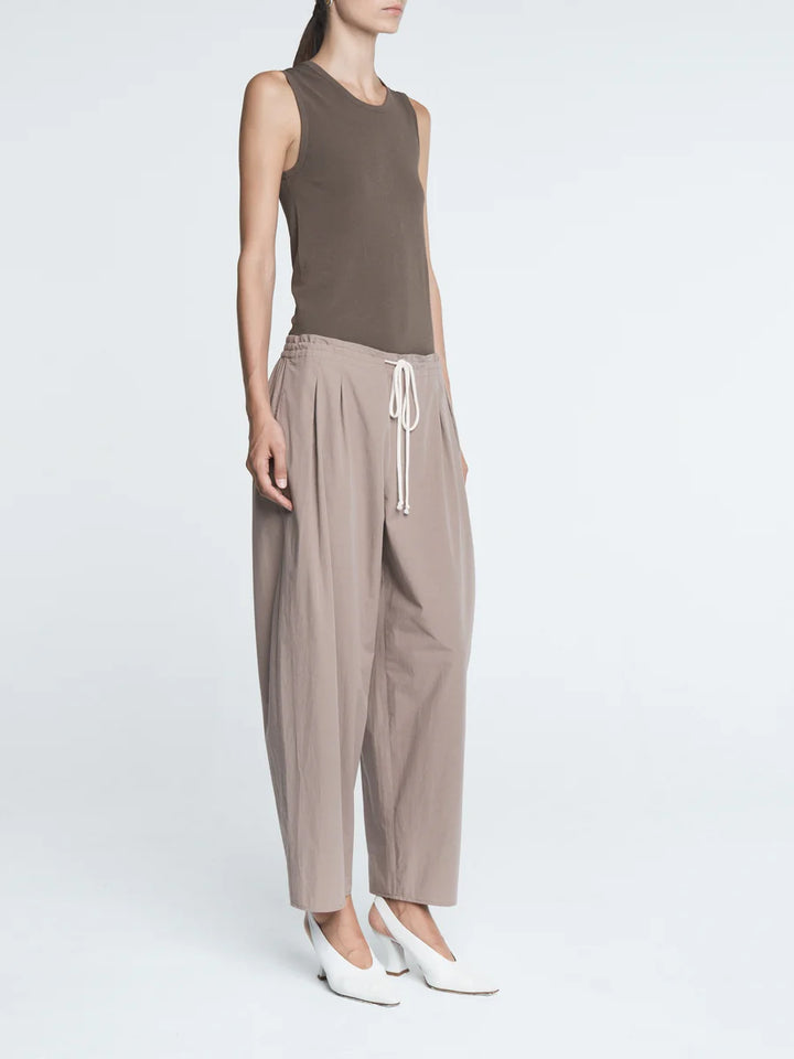 Woman wearing a brown sleeveless top and beige pants on a white background