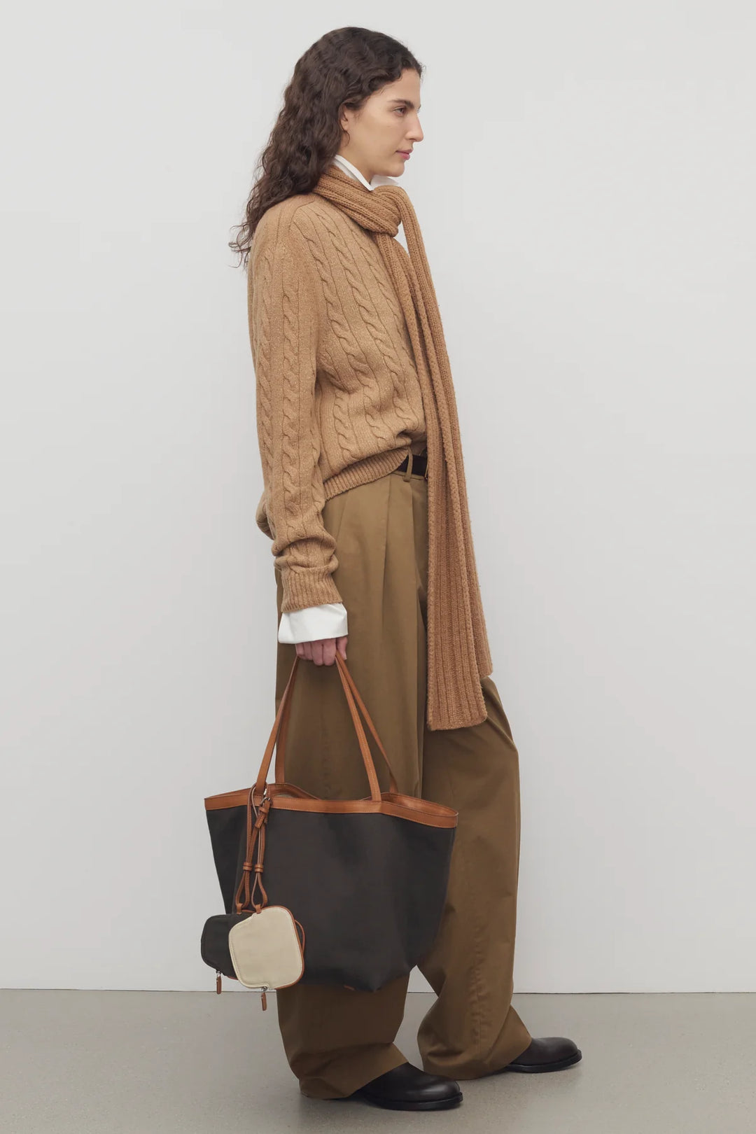 Woman wearing a brown sweater and scarf, holding a black and brown tote bag against a white background