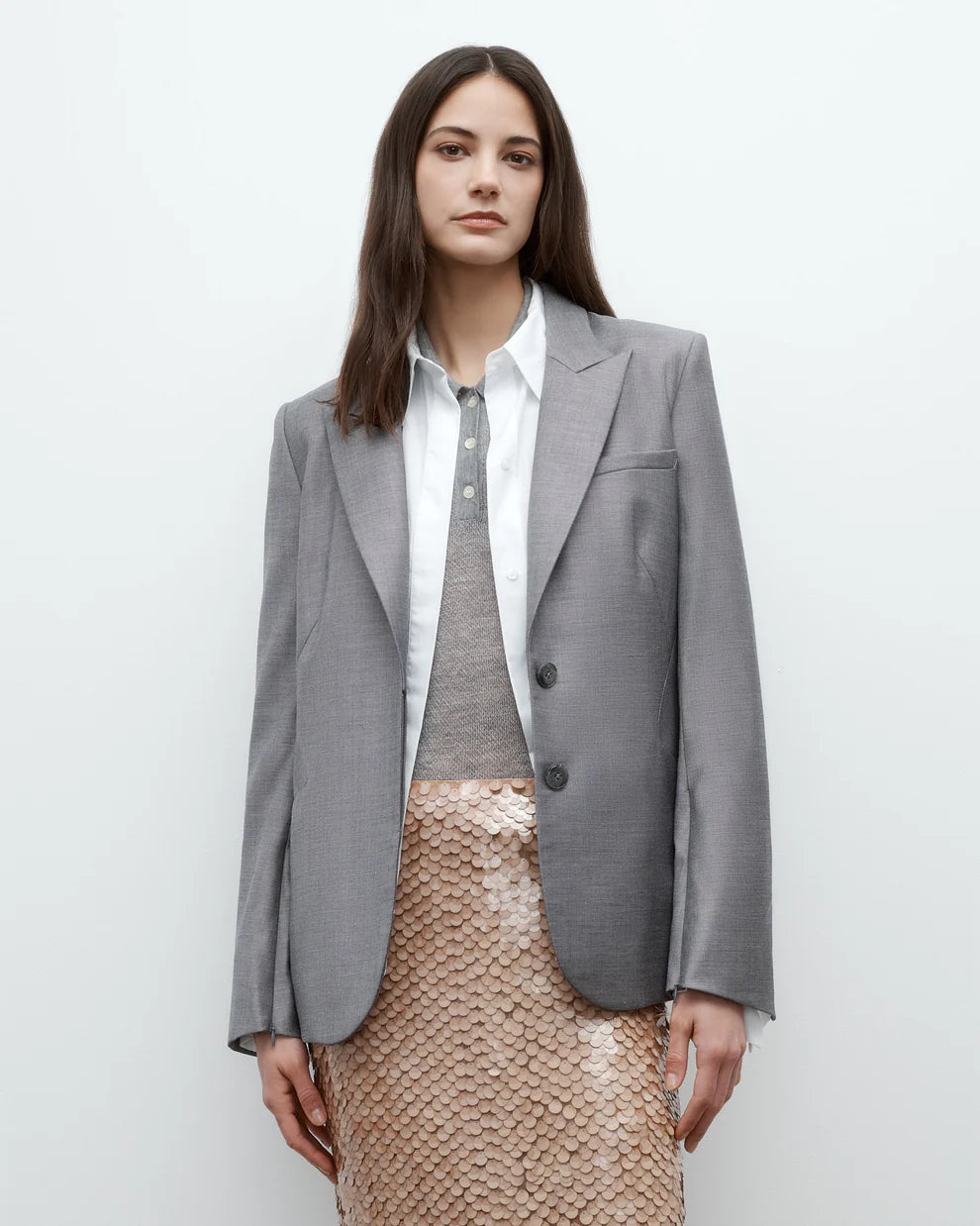 Woman wearing a gray blazer over a white shirt and gray sweater with a beige sequin skirt on a white background