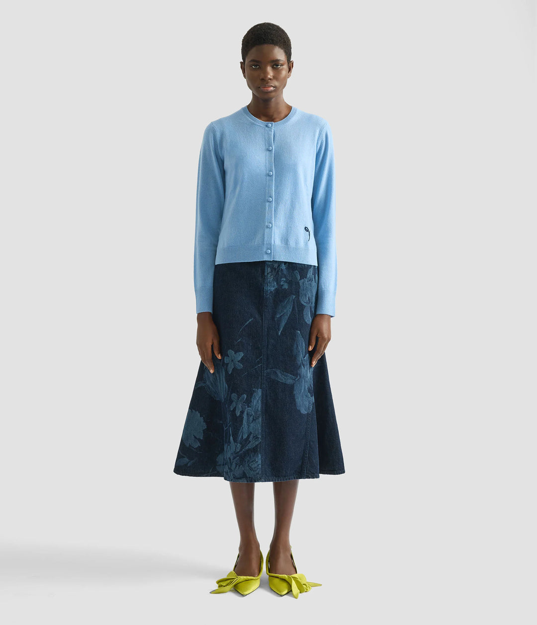 Woman wearing a light blue cardigan and dark blue floral skirt on a white background