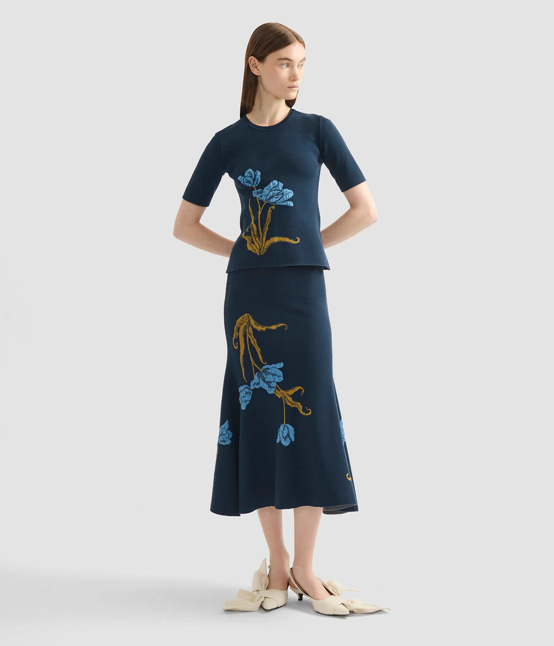 Woman wearing a navy blue dress with floral embroidery on a light gray background