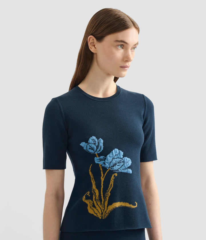 Woman wearing a navy blue sweater with floral embroidery on a light gray background