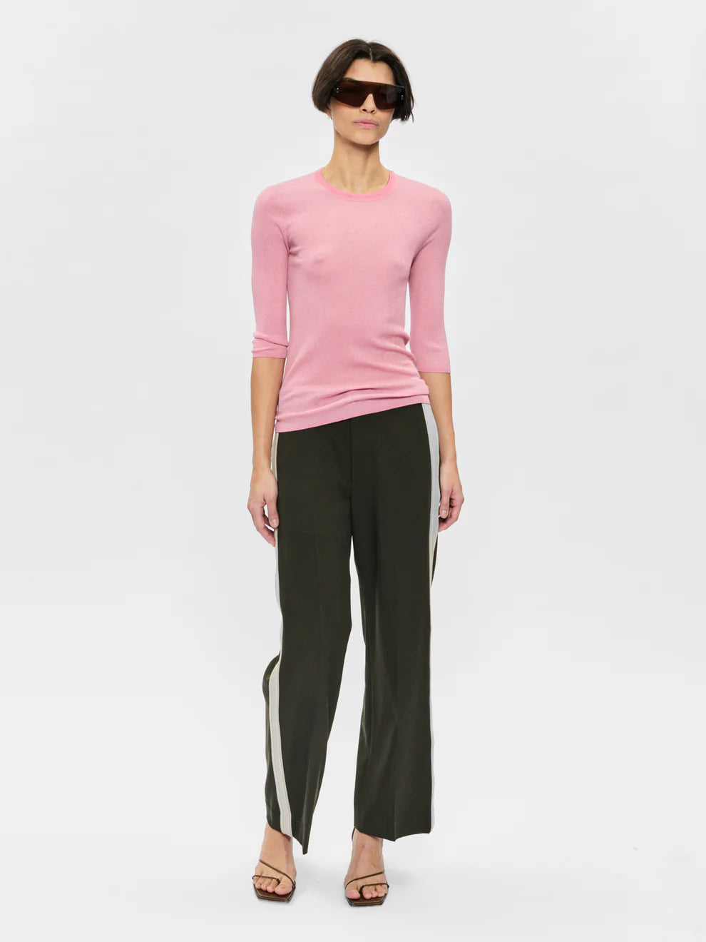Woman wearing a pink sweater and black pants with white stripes on a white background