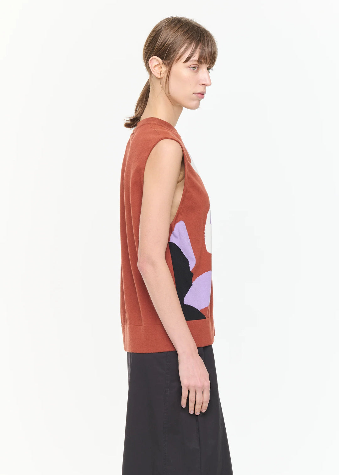 Woman wearing a sleeveless rust-colored top with abstract design on a white background