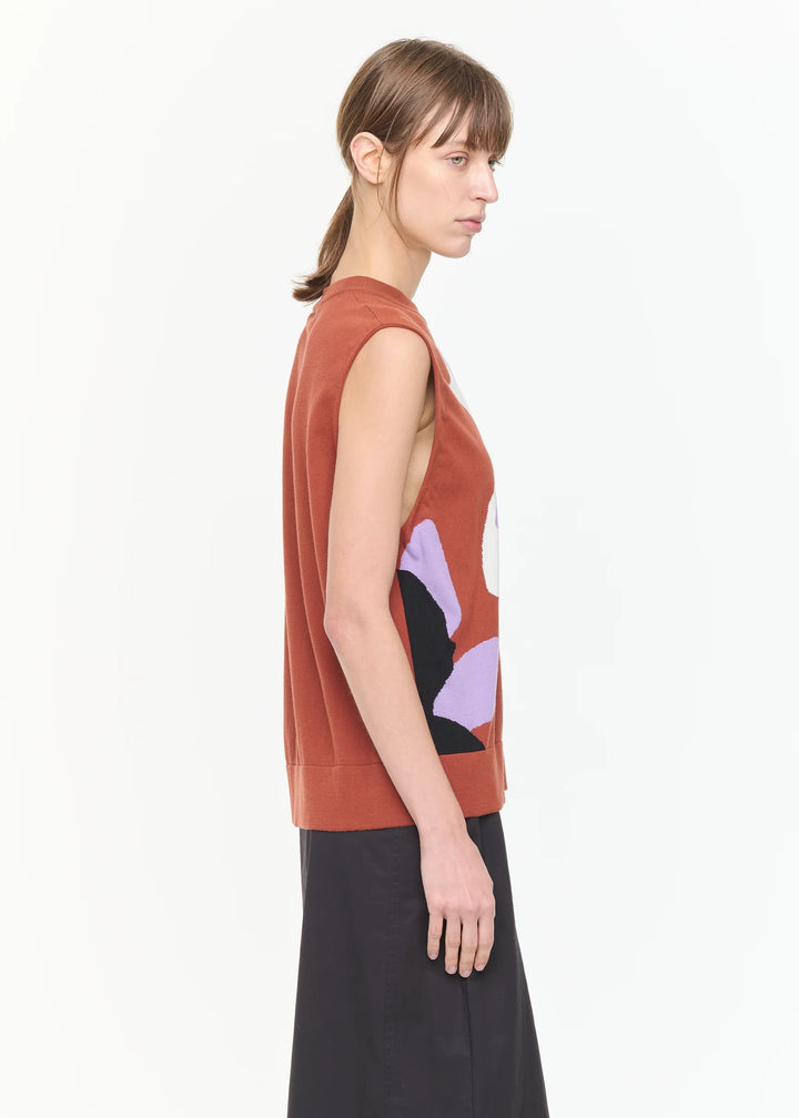 Woman wearing a sleeveless rust-colored top with abstract design on a white background