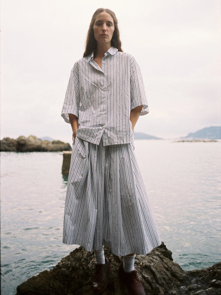 Woman wearing a striped outfit standing on a rock by a body of water.
