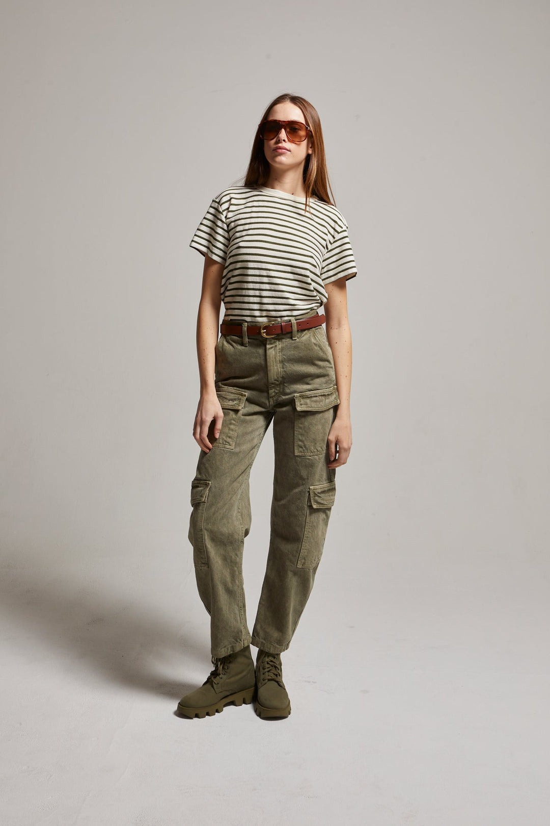 Woman wearing a striped shirt, cargo pants, and boots on a plain background