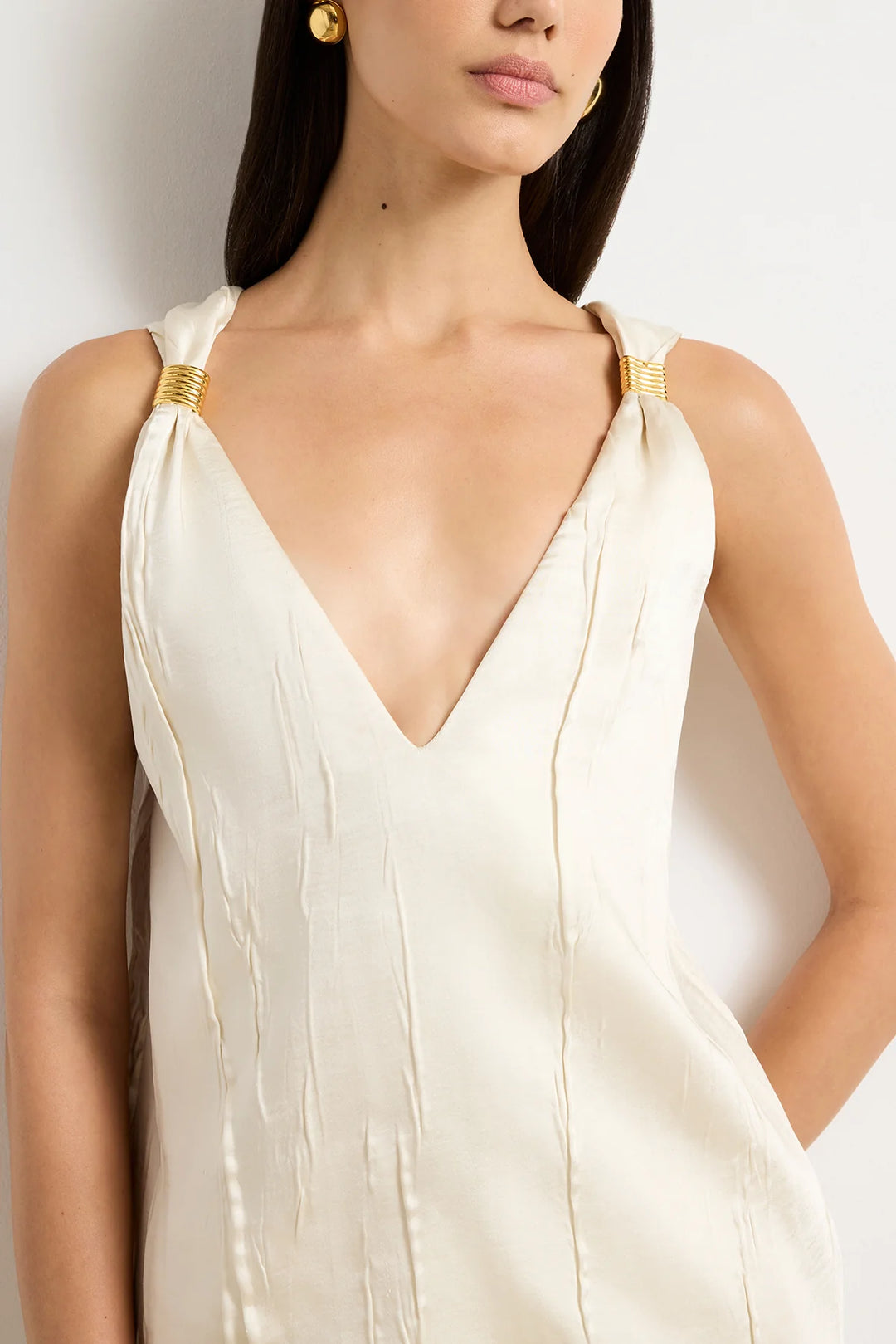 Woman wearing a white dress with gold straps against a plain background