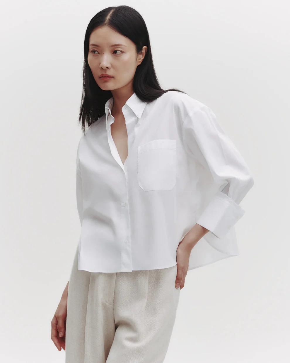 Woman wearing a white shirt and beige pants on a plain background