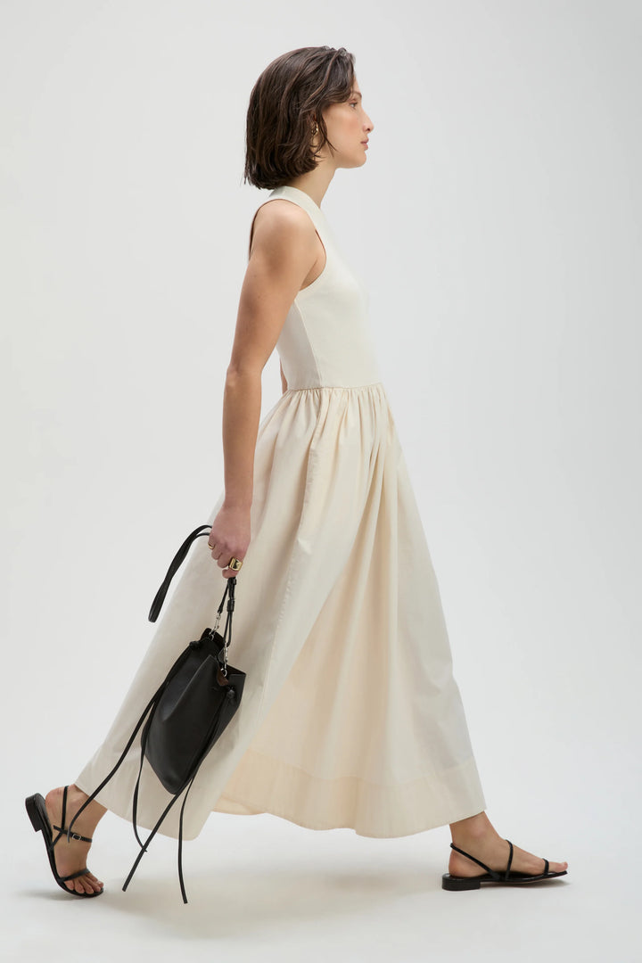 Woman wearing a white sleeveless top and beige skirt with a black handbag on a white background