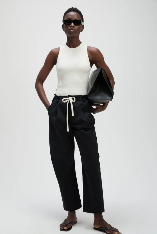 Woman wearing a white sleeveless top and black pants with a white background