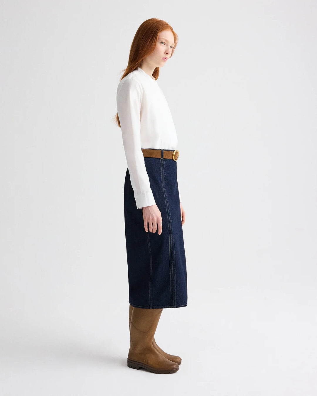 Woman wearing a white sweater, navy skirt, and brown boots on a white background