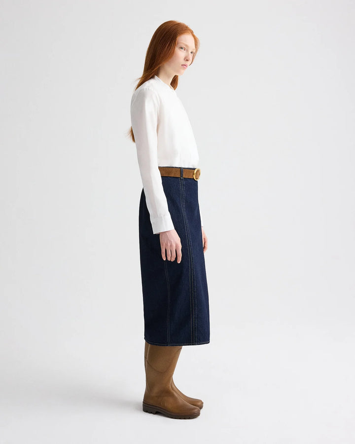 Woman wearing a white sweater, navy skirt, and brown boots on a white background
