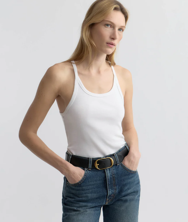 Woman wearing a white tank top and blue jeans against a plain background