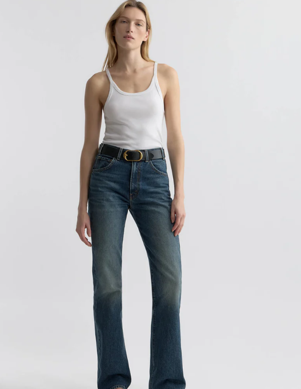 Woman wearing a white tank top and blue jeans on a light gray background